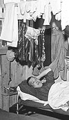 Manzanar Relocation Center, Manzanar, California. An evacuee resting on his cot after moving his belongings into this bare barracks room. An army cot and mattress are the only things furnished by the government. All personal belongings were brought by the evacuees, April 2, 1942. Photo: Department of the Interior. War Relocation Authority. Source: National Archives.