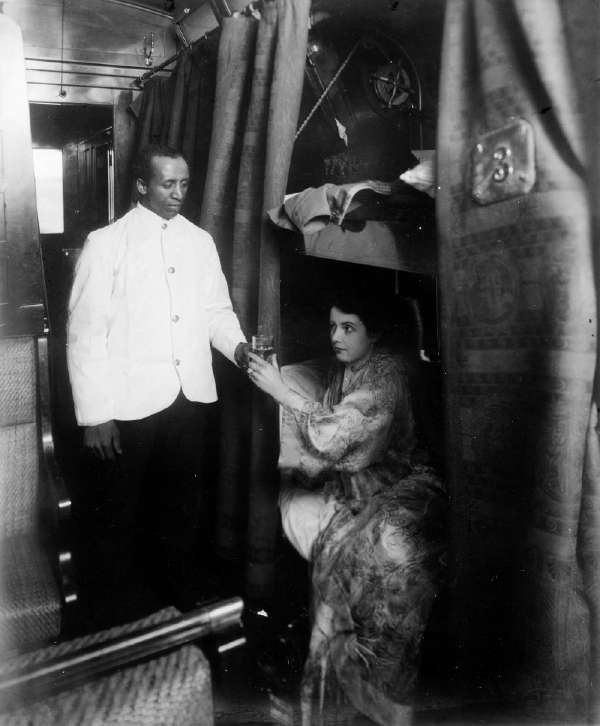 Porter Handing Young Woman A Glass Of Water In Railroad Sleeping Car